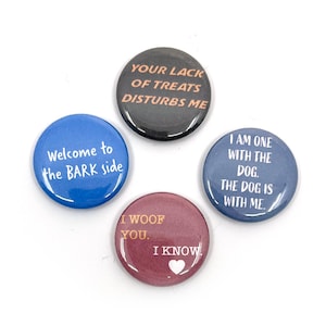 May include: Four round pinback buttons with humorous dog-themed phrases. The buttons are blue, black, and burgundy, with white text. Phrases include "Welcome to the BARK side" and "Your lack of treats disturbs me."