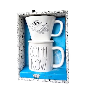 Puede incluir: Un juego de tazas de café de cerámica blanca con un diseño de Looney Tunes. La taza superior tiene un gráfico de Taz el Demonio de Tasmania, y la taza inferior dice "COFFEE NOW" en letras negras. El juego viene en una caja decorativa.