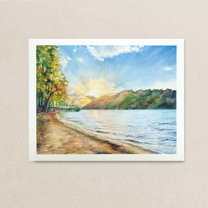 May include: Watercolor painting of a serene lakeside scene at sunset. The artwork depicts a sandy beach, calm water, and a tree-lined shore. The sky is a mix of blue and yellow, with the sun's rays breaking through the clouds.