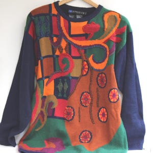 May include: A colorful sweater with a patchwork design. The sweater features a navy blue crew neck and sleeves, with a vibrant mix of orange, green, red, and brown geometric patterns and floral accents. The sweater is hanging on a wooden hanger.