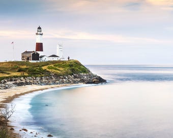 May include: A white and red lighthouse stands on a rocky cliff overlooking a calm, blue ocean. The lighthouse is surrounded by green grass and a sandy beach.