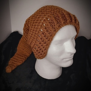 Puede incluir: Un gorro de punto de color marrón con una cola larga. El gorro está hecho con un patrón de punto sencillo y tiene un ajuste holgado.
