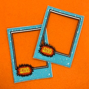 May include: Two blue and white photo frames with a white border and a black inner border. Each frame has a yellow and orange "Star Wars" logo in a comic book style.