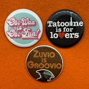 May include: Three round buttons with different designs. The first button is light blue with white text that says "Obi-Wan is Obi-Fun!" The second button is black with white text that says "Tatooine is for lovers" with a red heart. The third button is brown with yellow text that says "Zuvio is Groovio" and a cartoon alien.