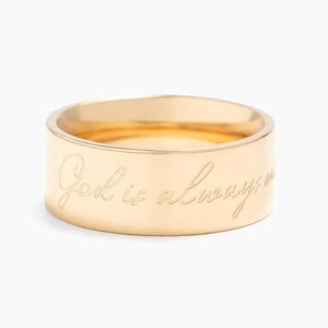 May include: A gold band ring with the inscription "God is always with you" engraved on the outside.