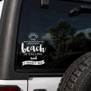 May include: White vinyl decal applied to a vehicle's rear window. The decal features the text "The beach is calling and I must go" with a sun and wave design. The decal is on a white vehicle.