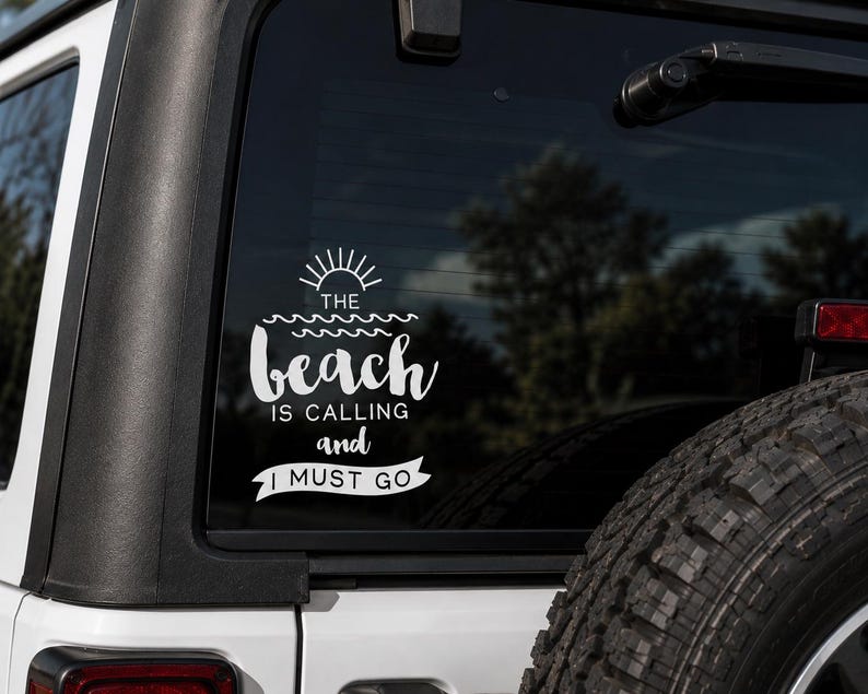 May include: White vinyl decal applied to a vehicle's rear window. The decal features the text "The beach is calling and I must go" with a sun and wave design. The decal is on a white vehicle.