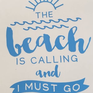 May include: A white background with blue text that reads "THE BEACH IS CALLING and I MUST GO." The design includes a sun, waves, and a banner. The text is in a handwritten style.