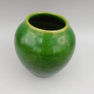 May include: A round, green ceramic vase with a glossy finish. The vase has a wide opening and a slightly lighter green rim. The overall shape is bulbous, and the color is a vibrant, solid green.