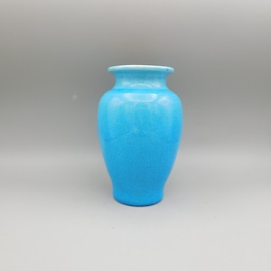 May include: A turquoise ceramic vase with a textured surface. The vase has a rounded body, a narrow neck, and a flared rim. The interior rim is white. The vase is a solid color and has a glossy finish.