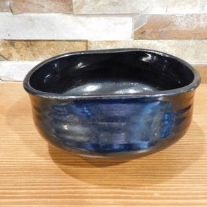 May include: A dark blue ceramic bowl with a slightly oval shape. The bowl has a glossy finish and is perfect for serving a variety of dishes.
