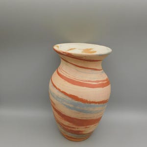May include: A decorative ceramic vase with a wide base and a flared top. The vase is painted with a swirling pattern of peach, orange, and blue brushstrokes. The interior of the vase is a light cream color.