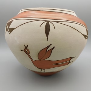 May include: A white ceramic pot with a brown and orange bird design. The pot has a wide mouth and a rounded body.