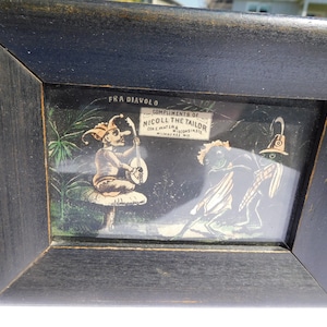 May include: A framed black and white illustration of a jester playing a musical instrument and a green creature with a hat. The illustration is titled "Fra Diavolo" and includes the text "Compliments of Nicoll the Tailor, Cor. E. Water & Wisconsin, Milwaukee, Wis."