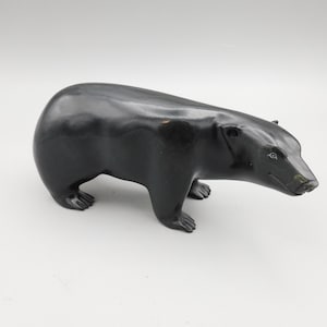 May include: A black bear figurine with a smooth, glossy finish. The bear is depicted in a standing position, with its paws visible. The sculpture has a rounded body and a detailed face, showcasing a realistic representation of the animal.