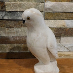 May include: White carved owl figurine with black eyes and a detailed design. The owl is standing on a base and is made of a smooth, white material.