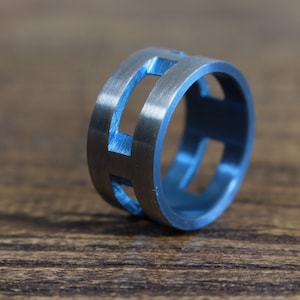 May include: A silver ring with a blue inlay and a geometric design. The ring has a brushed finish and is made of metal.