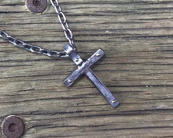 May include: A silver chain necklace with a black metal cross pendant. The cross has small gold accents.
