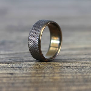 Op de afbeelding: Een zilveren ring met een getextureerde band en een gouden binnenband.