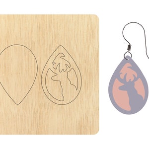 Puede incluir: Una plantilla de madera para elaborar un par de pendientes. La plantilla incluye dos formas: una lágrima y una lágrima con una silueta de ciervo. Se muestra un par de pendientes terminado con una silueta de ciervo rosa sobre un fondo morado claro.