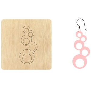 Puede incluir: Una plantilla de madera cortada con láser para hacer pendientes. La plantilla muestra un diseño de cinco círculos superpuestos. Los pendientes terminados se muestran en rosa.