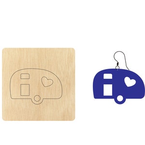 Puede incluir: Un recorte de madera de una caravana con un corazón en el lateral. El recorte está sobre un fondo de madera. También hay un pendiente de caravana azul con un corazón en el lateral.