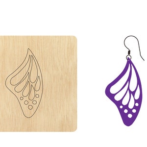 Puede incluir: Una plantilla de madera para hacer un par de pendientes. La plantilla tiene forma de ala de mariposa con un diseño recortado. La plantilla se muestra junto a un par de pendientes de ala de mariposa de color morado.