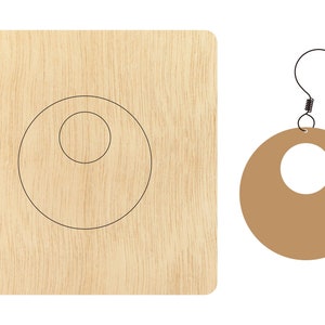 Puede incluir: Una plantilla de madera para hacer un par de pendientes. La plantilla muestra un círculo con un círculo más pequeño cortado en el centro. Los pendientes son marrones y tienen un diseño simple de aro.