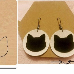 Puede incluir: Un juego de dos plantillas de madera para hacer pendientes. Las plantillas miden 10 cm de ancho y 10 cm de alto. Las plantillas incluyen un círculo y una forma de cabeza de gato. Los pendientes terminados tienen un diámetro de 5 cm y presentan una silueta de gato negro sobre un fondo blanco.