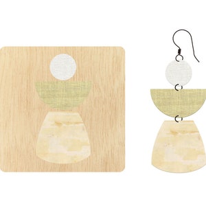 Puede incluir: Un par de pendientes geométricos con fondo de madera. Los pendientes están hechos de tres piezas: un círculo blanco, una media luna verde claro y una media luna beige. Los pendientes están suspendidos de un alambre negro.