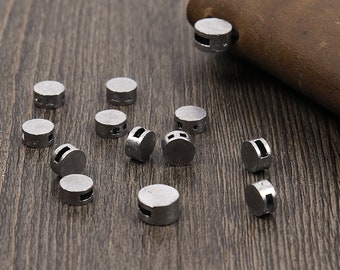 May include: A collection of silver-colored metal lead-free solder bullet snaps. The snaps are round and have a small hole in the center. They are scattered on a wooden surface.