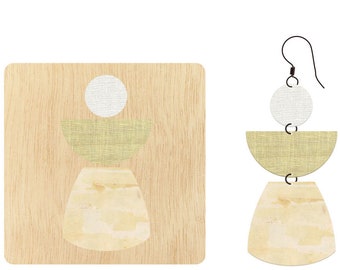 May include: A pair of geometric earrings with a woodgrain background. The earrings are made of three pieces: a white circle, a light green crescent, and a beige crescent. The earrings are suspended from a black wire.