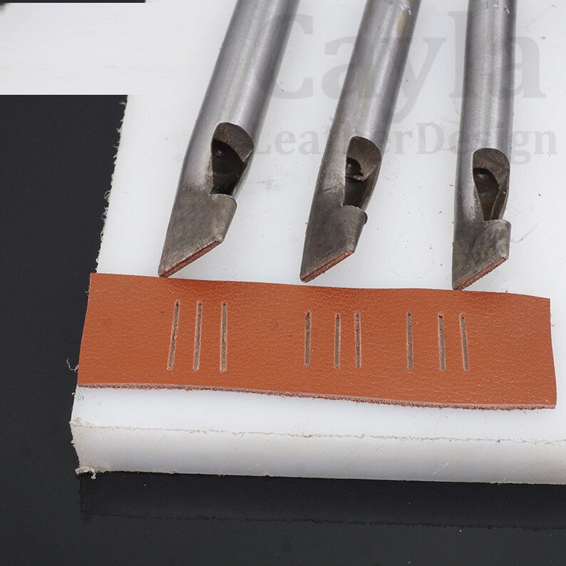 May include: Three metal leather stitching tools with a brown leather strip showing the stitching pattern created by the tools.