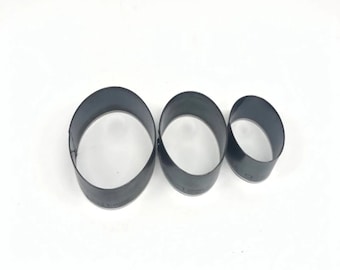 May include: Three oval-shaped metal leather craft tools of varying sizes. The tools are dark gray and have a smooth, rounded edge. They are arranged in a row on a white surface.