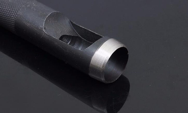 May include: A close-up of a black metal hole punch with a silver rim around the cutting edge. The punch is designed to create round holes in materials like leather or paper.
