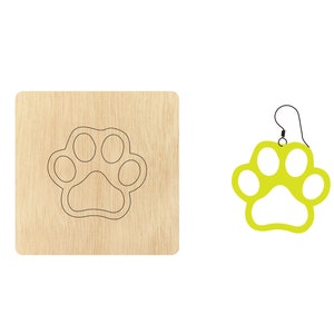 Könnte beinhalten: Eine Holzvorlage zum Basteln einer Pfotenabdruck-Ohrring. Die Vorlage ist hellbraun und hat einen schwarzen Umriss eines Pfotenabdrucks. Neben der Vorlage ist ein grüner Pfotenabdruck-Ohrring zu sehen.