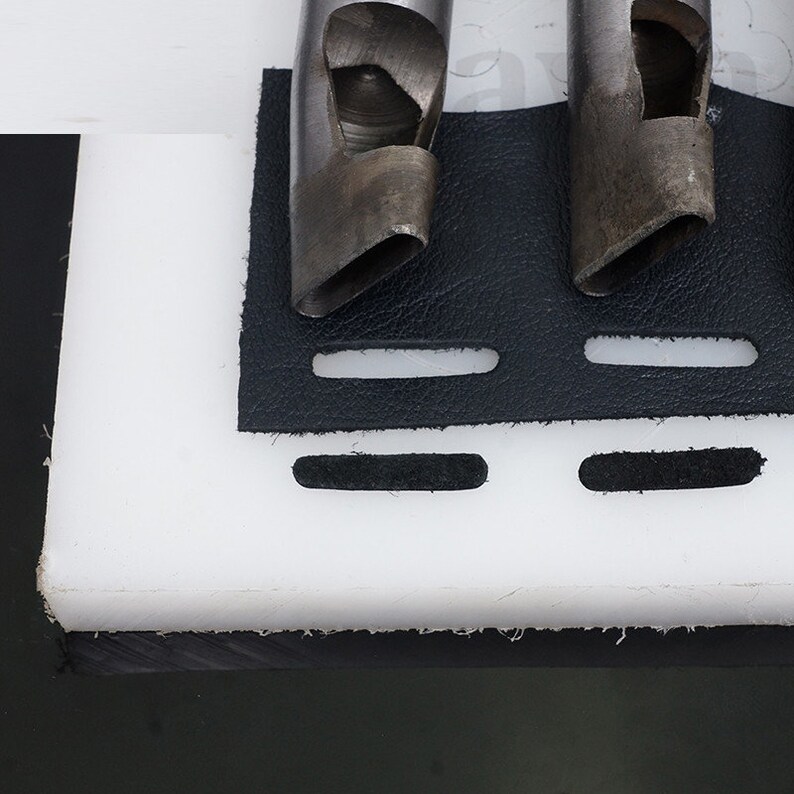 May include: Three metal leather hole punch tools on a black leather surface with a white cutting mat underneath.