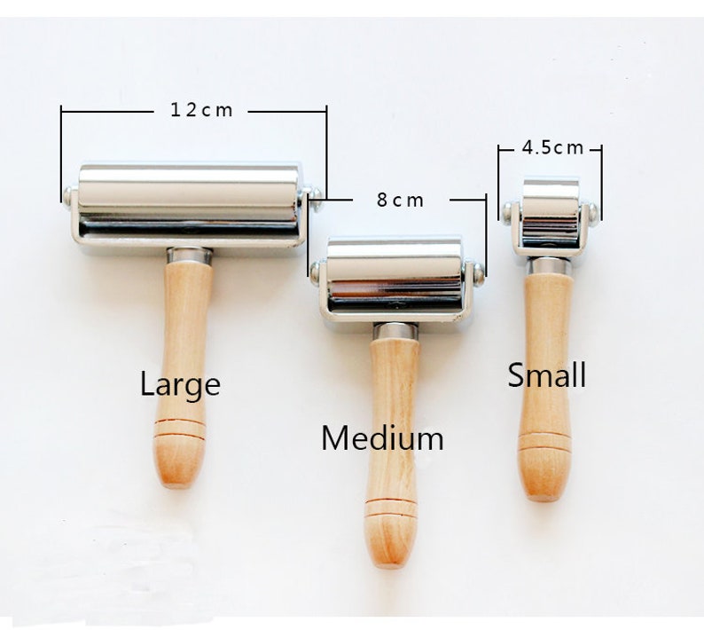 May include: Three metal and wood craft rollers in varying sizes. The largest roller is 12 cm wide, the medium roller is 8 cm wide, and the smallest roller is 4.5 cm wide. Each roller has a wooden handle.