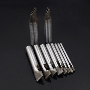 May include: A set of 11 leather hole punches, including two long punches with pointed tips and nine shorter punches with various shaped openings. The punches are made of metal and have a silver finish.