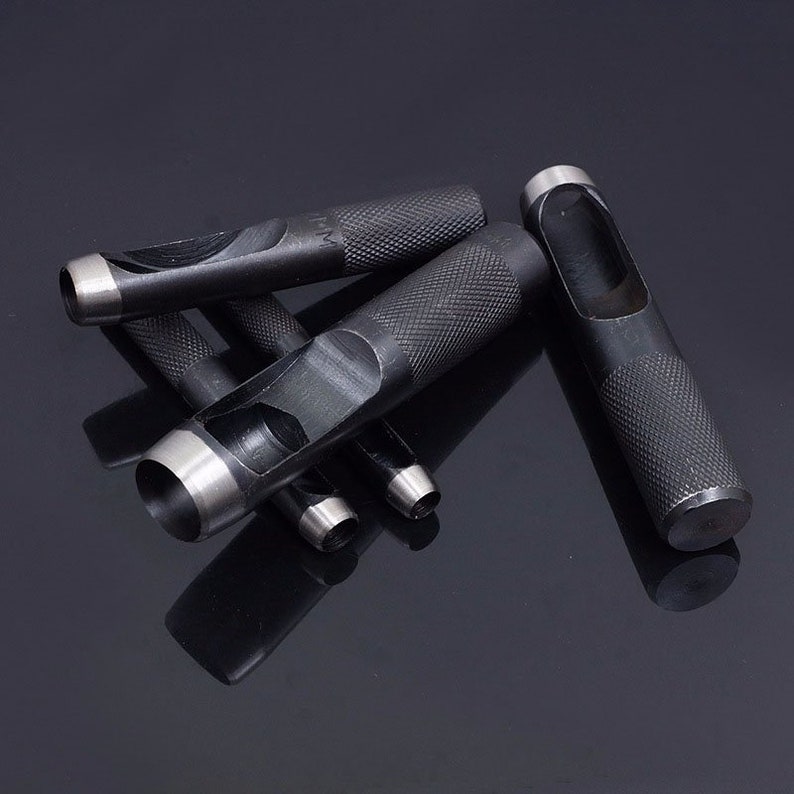 May include: A set of five black metal hole punch tools with different sized circular holes. The tools have a textured grip and are arranged on a black surface.