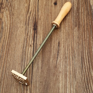 May include: A brass stamp with a wooden handle. The stamp has a rectangular shape and a design on the face. The handle is attached to the stamp with a threaded rod.