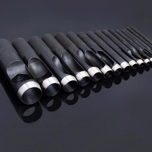 May include: A set of 18 black metal hole punches with silver edges, arranged in order of size from largest to smallest.
