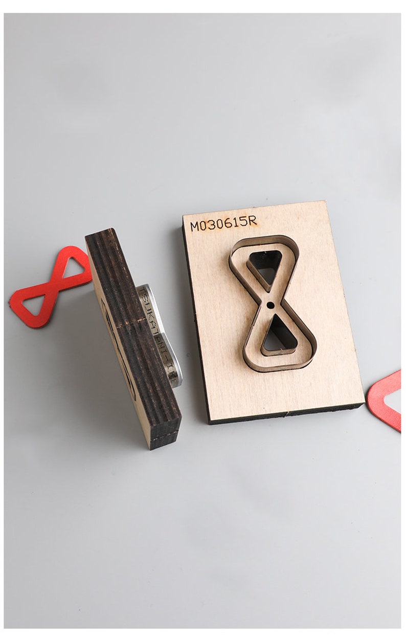 Pu&ograve; includere: Un modello di fustellatura in legno con il numero "M030615R" stampato su di esso. Il modello ha la forma di un simbolo di infinito con un simbolo di infinito pi&ugrave; piccolo all'interno. Il modello &egrave; su una superficie grigia.