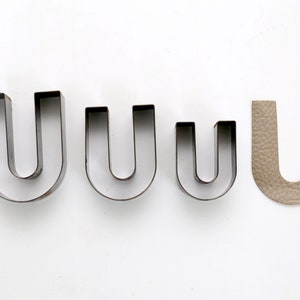 May include: Four metal cookie cutters shaped like the letter U, in decreasing sizes, and a brown leather cutout of the letter U.