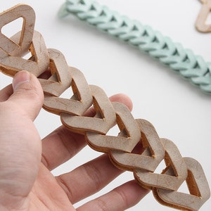 Pu&ograve; includere: Un braccialetto a catena in pelle marrone con un design triangolare. Il braccialetto &egrave; realizzato con pi&ugrave; pezzi di pelle intrecciati per formare una catena.