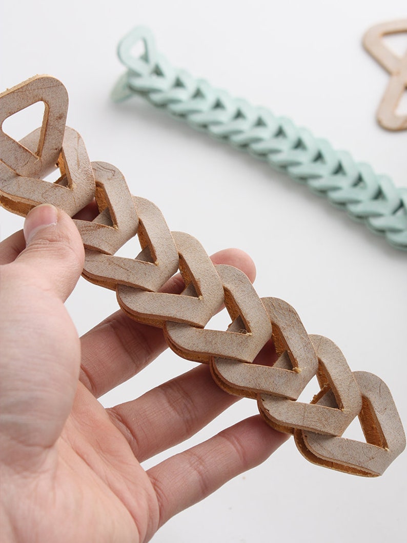 Pu&ograve; includere: Un braccialetto a catena in pelle marrone con un design triangolare. Il braccialetto &egrave; realizzato con pi&ugrave; pezzi di pelle intrecciati per formare una catena.