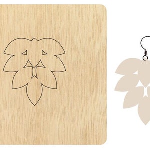 Puede incluir: Una plantilla de madera cortada con láser para hacer pendientes. La plantilla tiene forma de hoja con un diseño geométrico. La plantilla se muestra junto a un par de pendientes hechos con la plantilla. Los pendientes son de color beige claro.