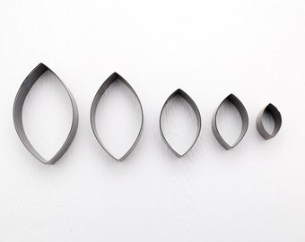 May include: Five metal cookie cutters in the shape of leaves, arranged in order of size from largest to smallest. The cutters are silver in color and have a smooth, polished finish.