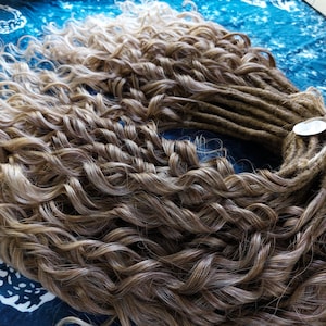 May include: A bundle of long, curly hair extensions in shades of brown and blonde. The hair is arranged in a circle, with the ends of the strands gathered together in the centre.
