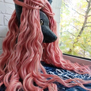 May include: A black and gray furry animal head with long, pink, wavy hair. The hair is styled in a side part and falls down the side of the head.